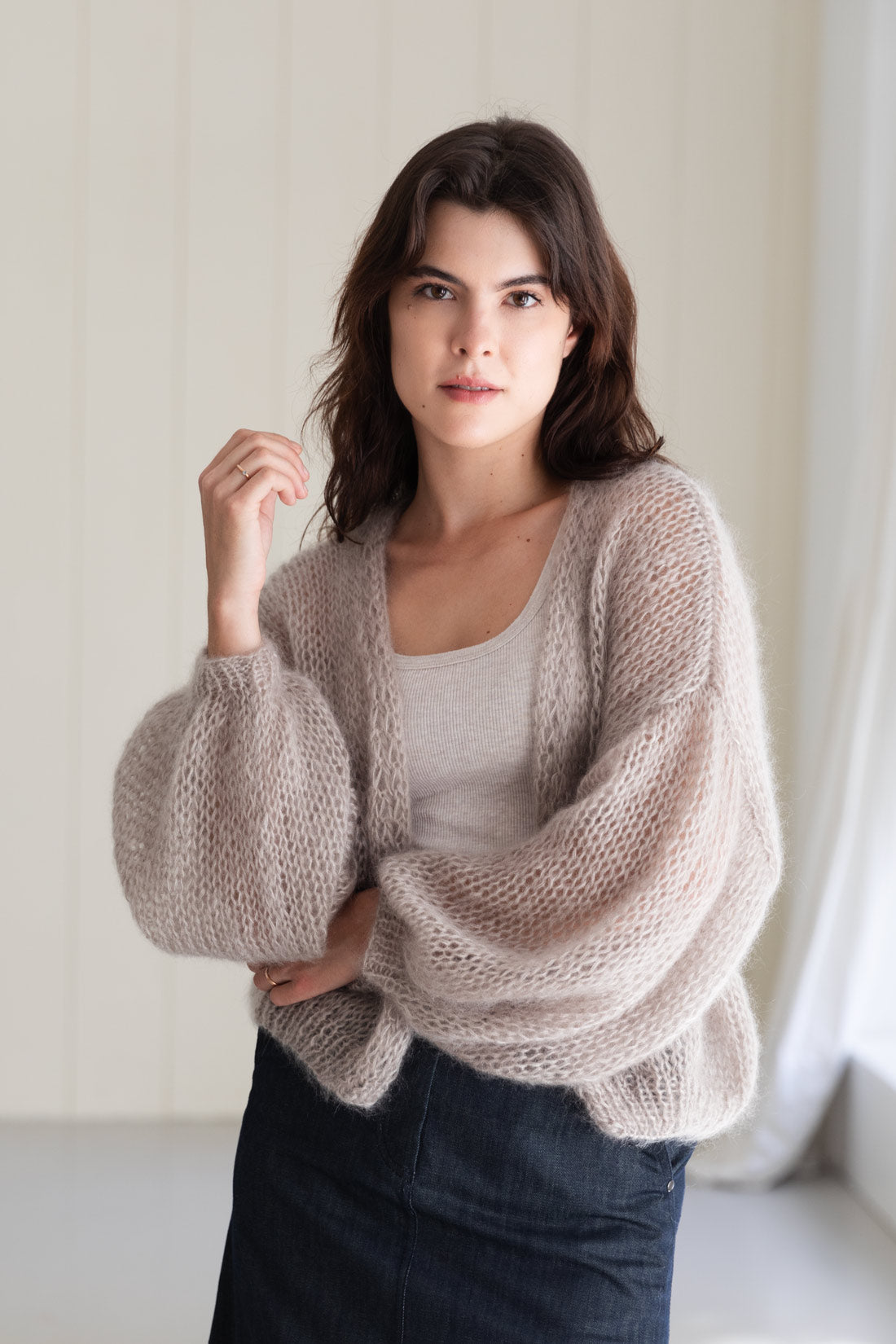 A woman wearing an airy mohair cardigan in a pearl-beige colour, styled over a light top and a dark denim skirt.