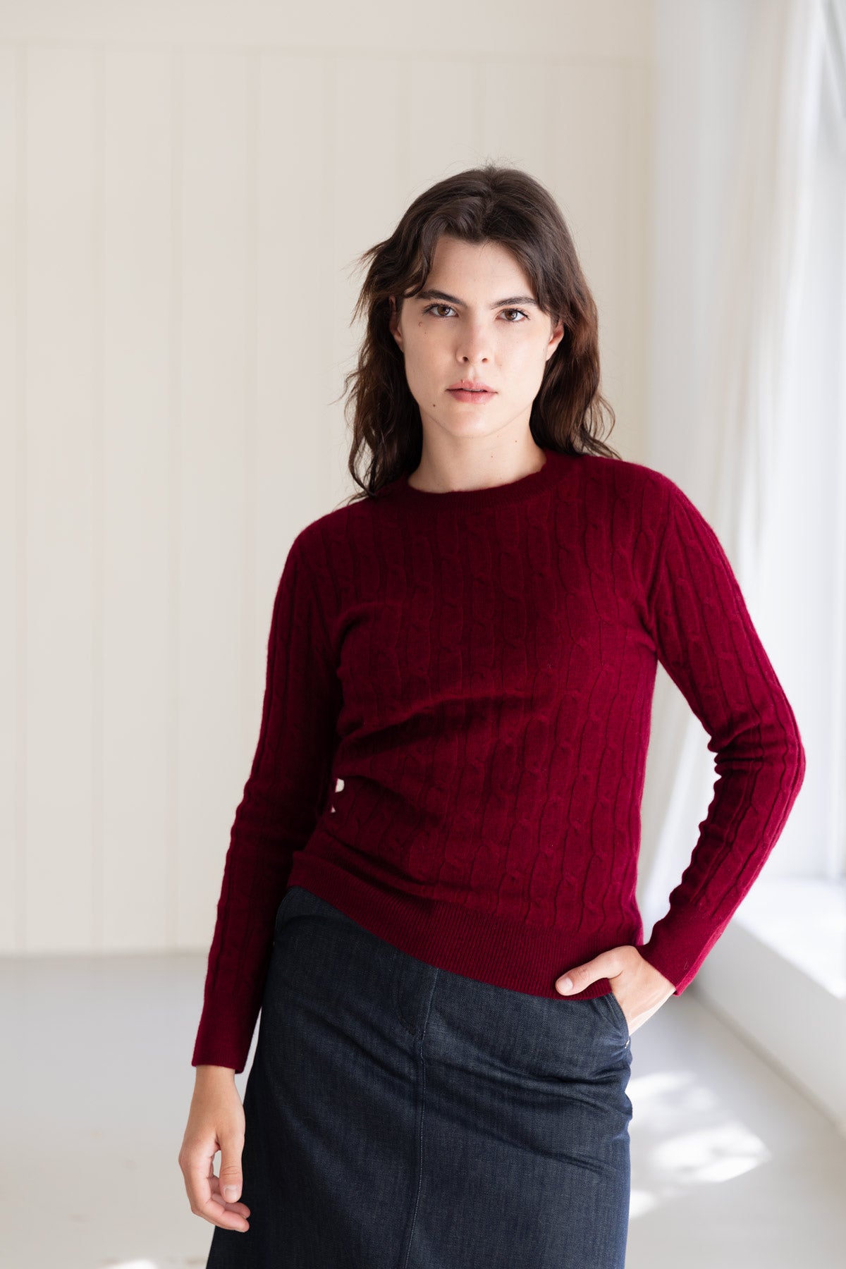 A woman wearing a dark red cable-knit cashmere sweater and a dark denim skirt. 