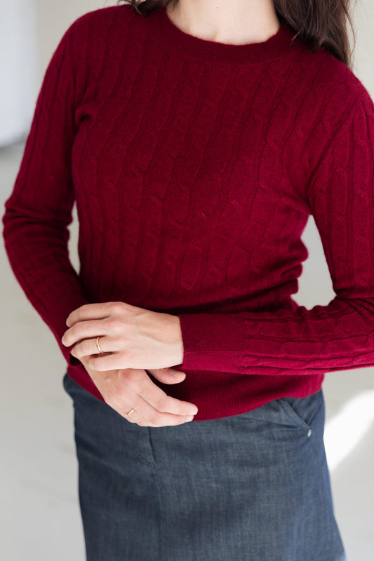 Close-up of a woman wearing a deep burgundy cable-knit cashmere sweater paired with a dark denim skirt.