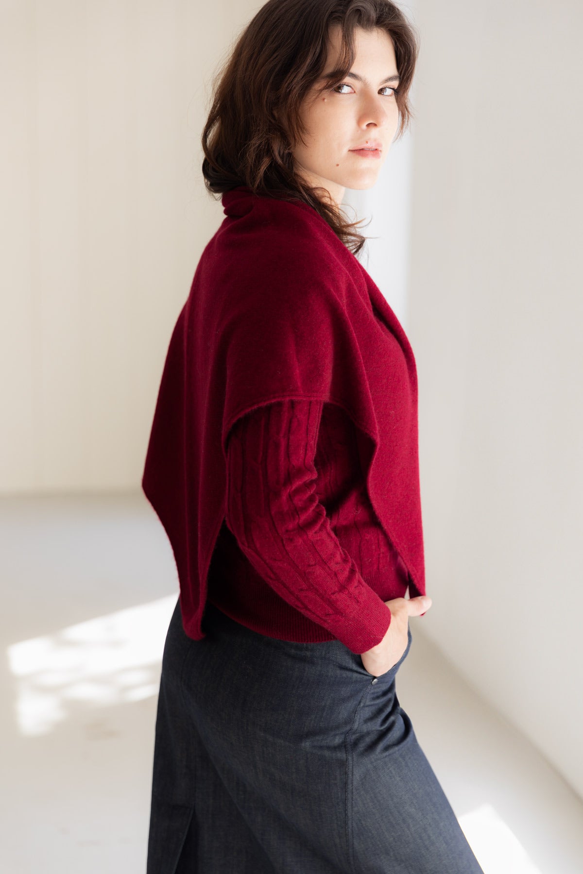 A woman wearing a deep burgundy cashmere triangle scarf over a matching cashmere sweater, paired with a dark denim skirt.