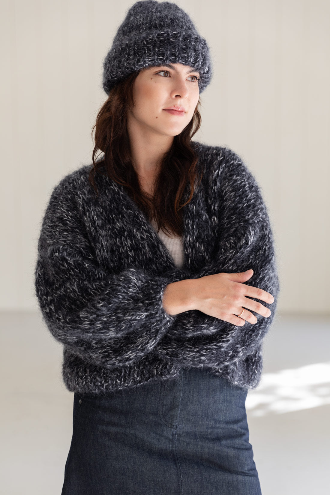 A woman wearing a chunky mohair beanie and a matching mohair cardigan in black and white colour, paired with a dark denim skirt.