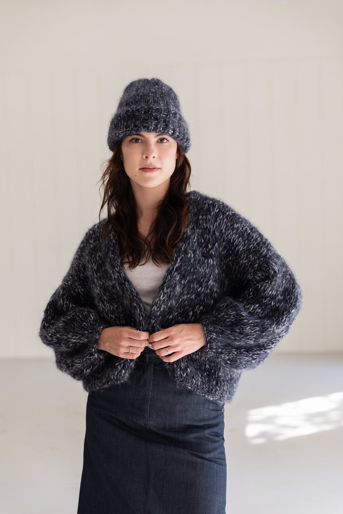A woman wearing a chunky mohair beanie in moulinee black and white, and a matching mohair cardigan, styled with a white top and dark denim skirt.