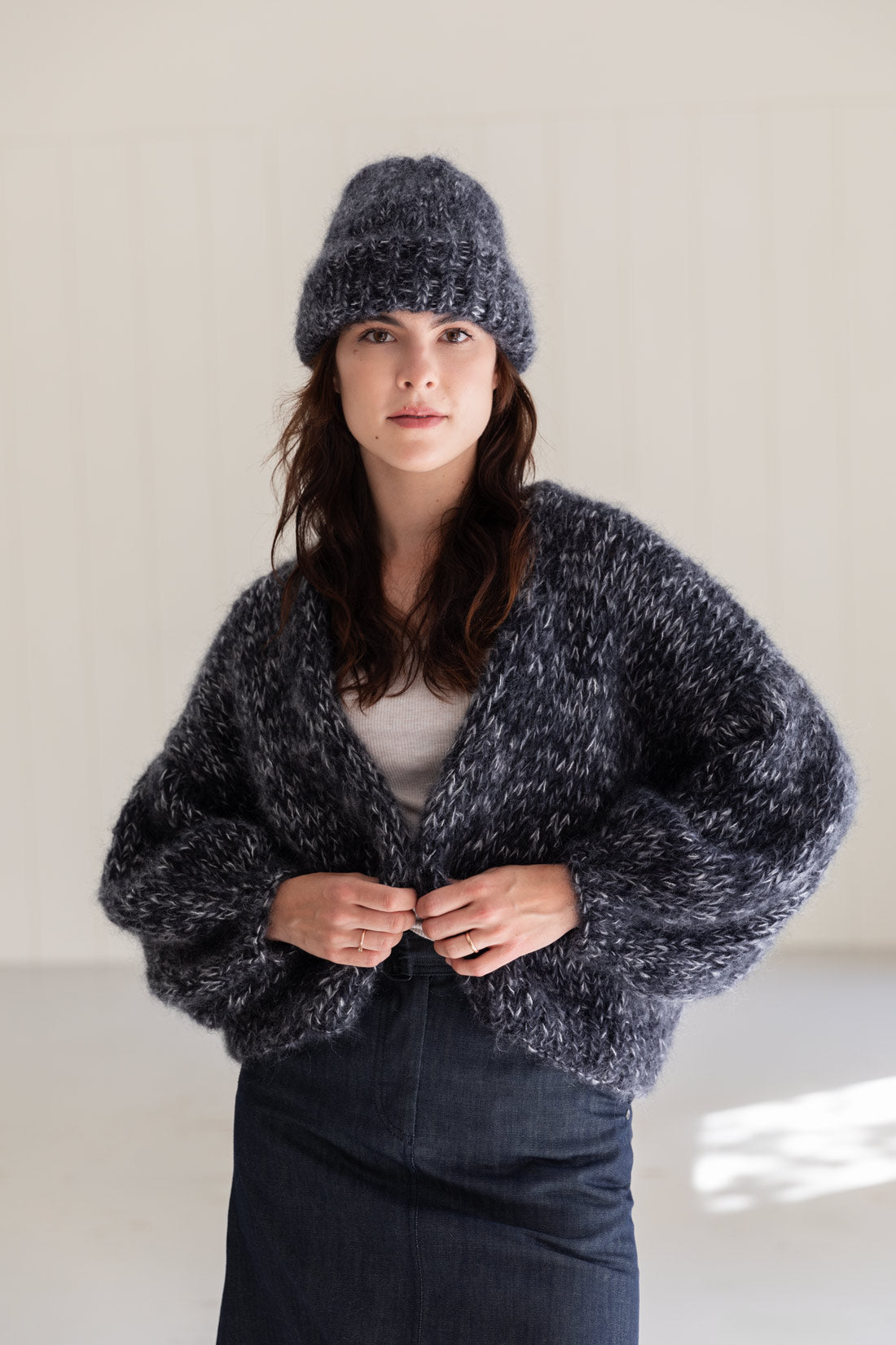 A woman wearing a chunky mohair beanie and a matching oversized mohair cardigan, standing against a light neutral indoor wall.