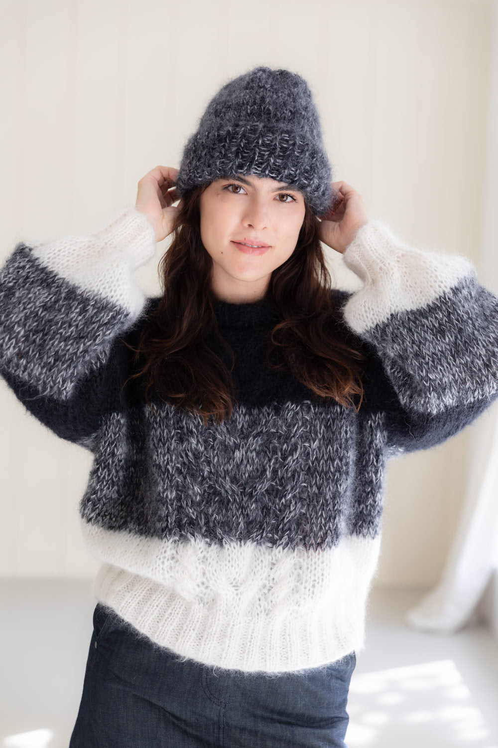 A woman wearing a chunky mohair beanie and a matching striped sweater in dark grey and off-white.