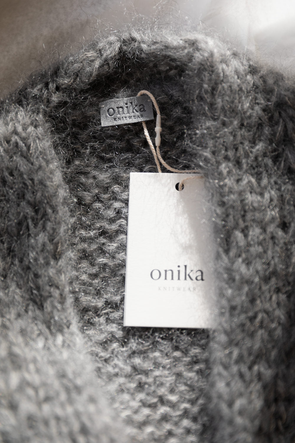 Close-up of a chunky mohair cardigan in grey, with a brand tag Onika Knitwear attached inside the collar.