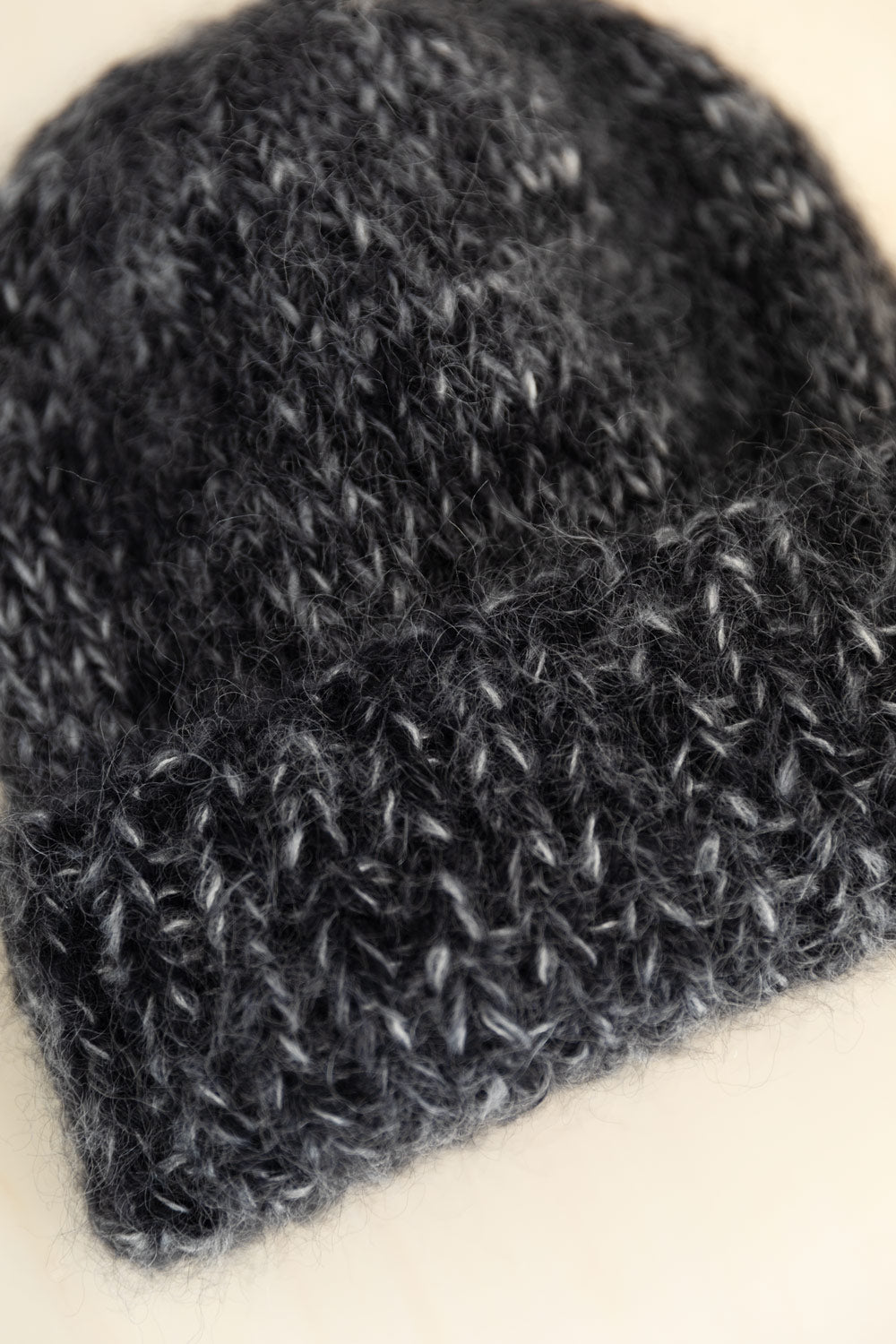 A close-up of a mohair beanie hat with a fuzzy texture, resting on a light cream background.