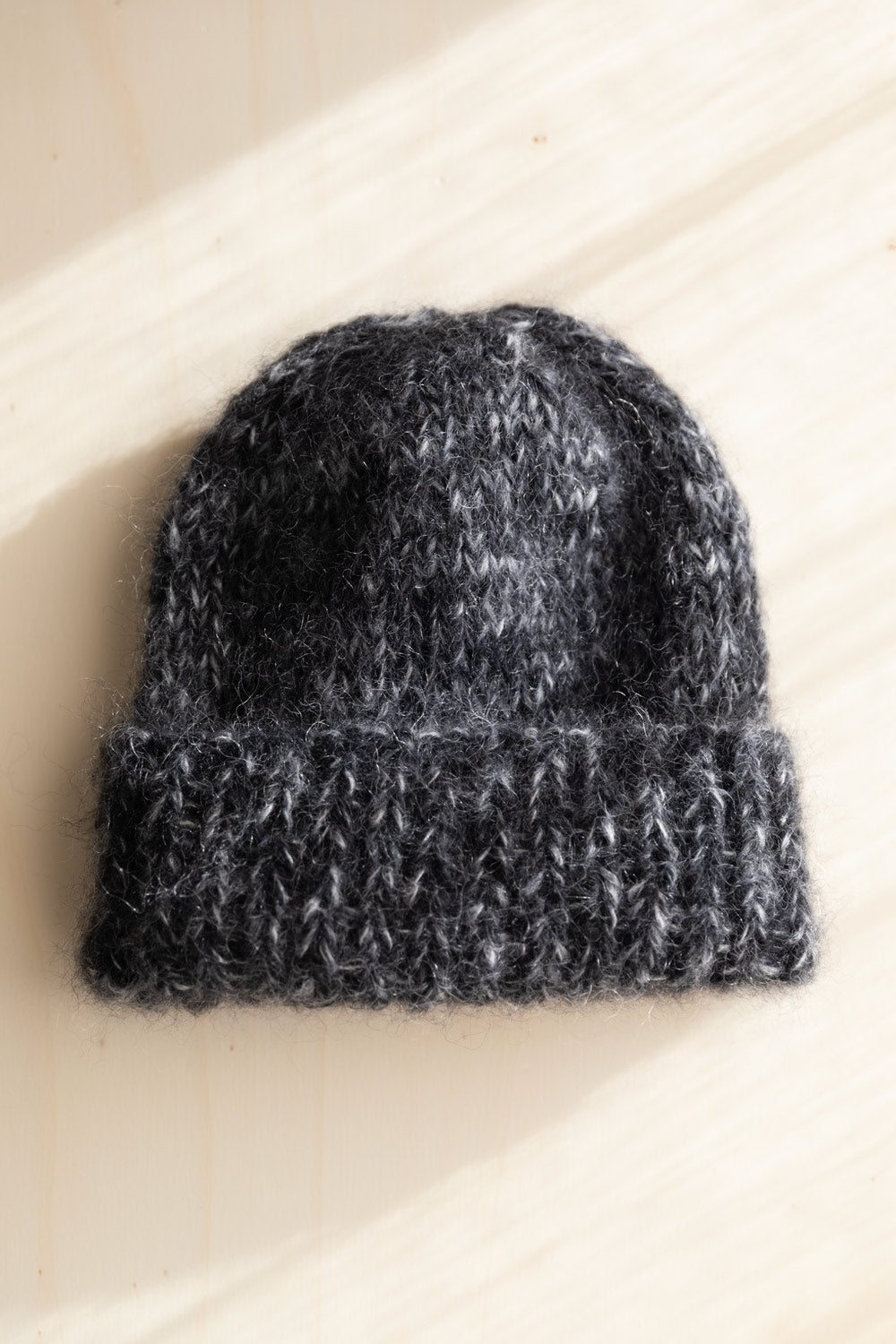 Mohair beanie in moulinee black and white, resting on a light beige wooden surface with soft diagonal shadows.
