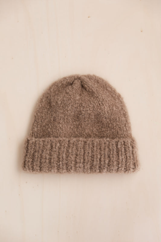 A bouclé cashmere beanie in taupe colour on a light beige surface
