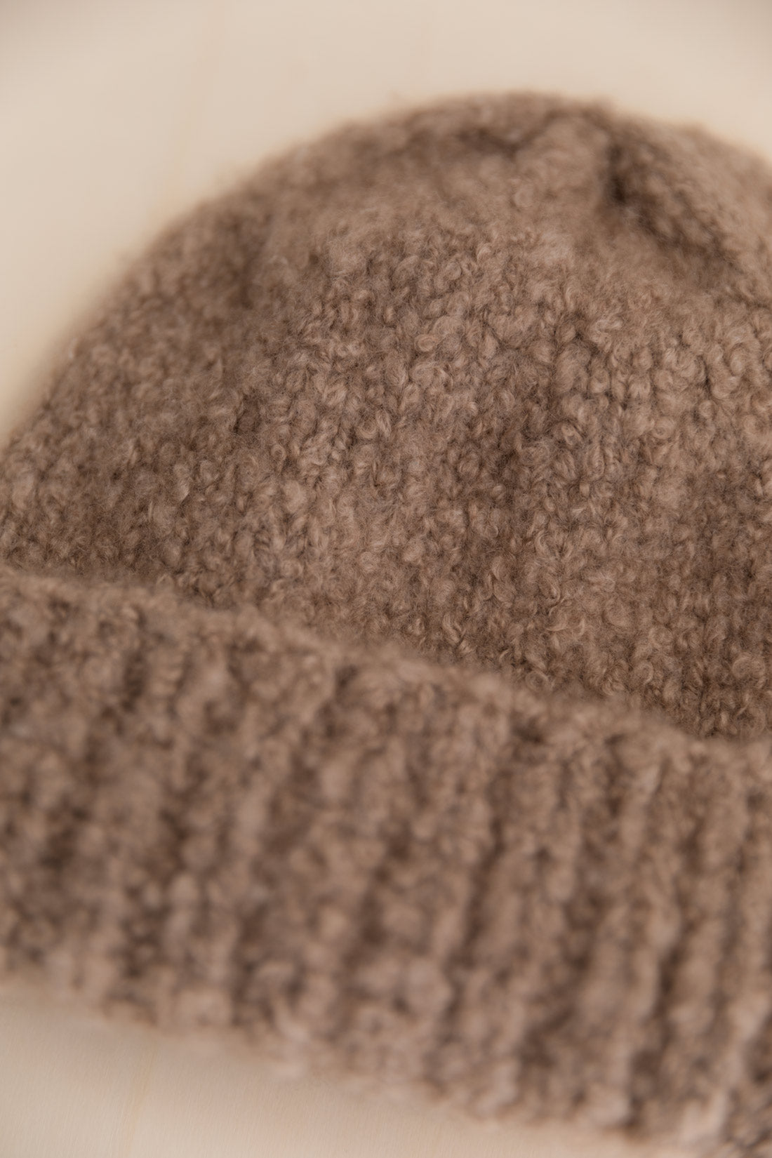 A close-up of a cashmere bouclee beanie in taupe colour, with a soft texture