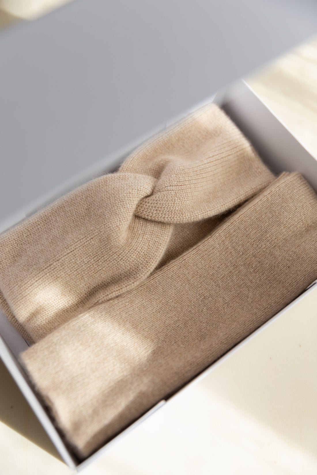 Cashmere headband and arm-warmers in a soft beige colour, both displayed inside a white gift box.