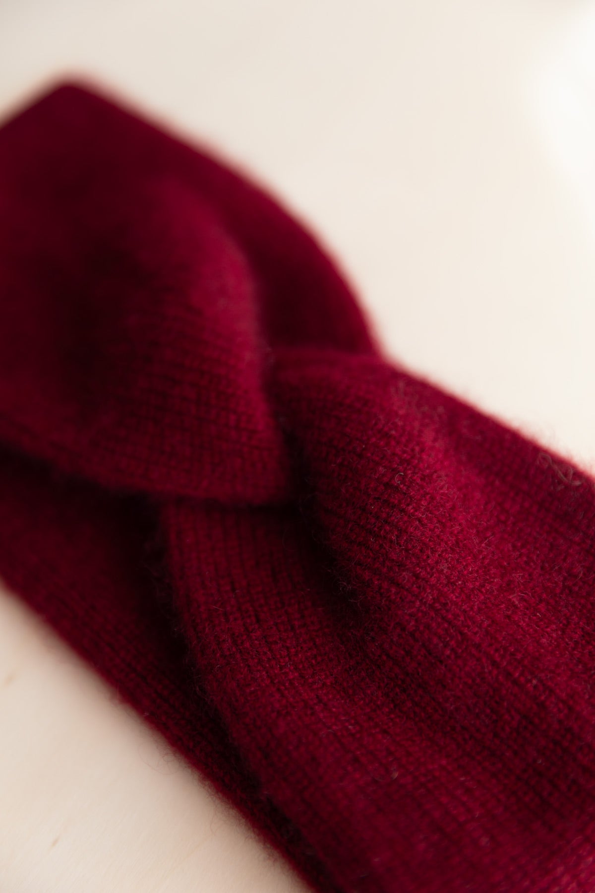 A close-up of a burgundy cashmere headband with a twisted knot detail, shown on a plain off-white background.