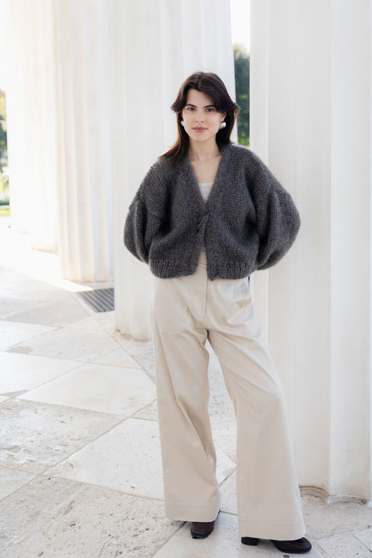 Woman wearing a dark gray cardigan and beige pants standing in front of white columns.