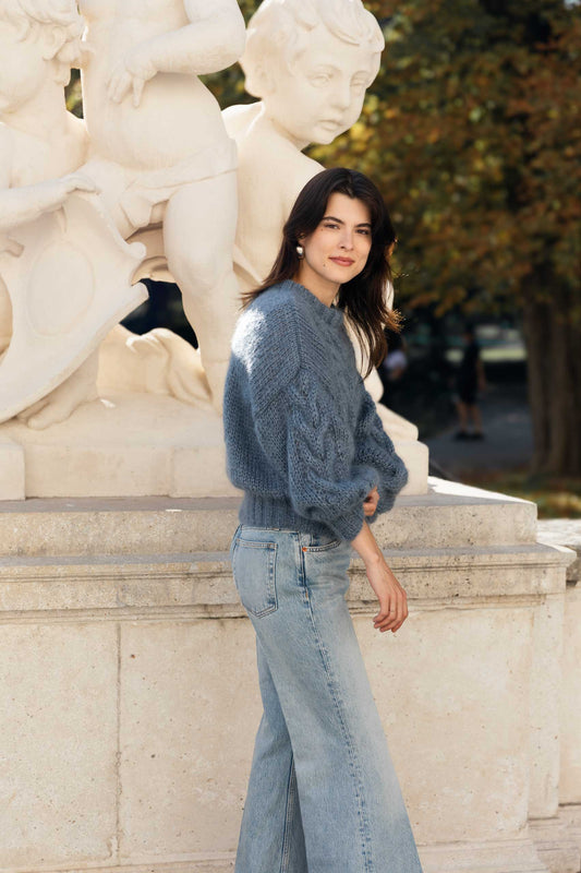 Woman wearing a blue mohair sweater and matching blue jeans standing in front of classical statues.