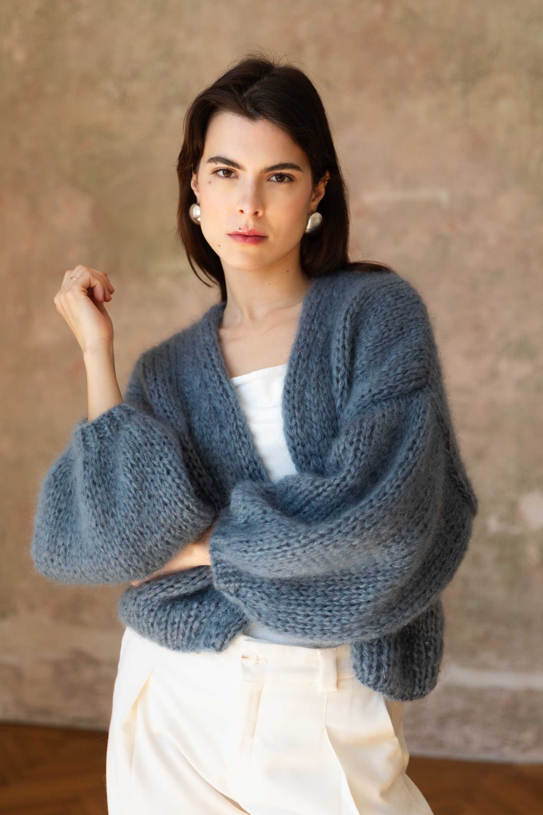 Woman wearing a handmade blue mohair cardigan against a neutral background