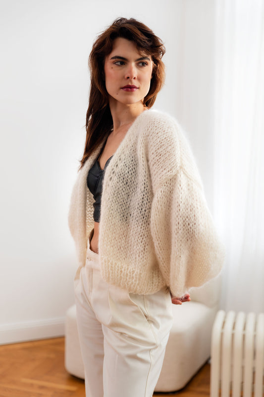 Woman wearing a white mohair cardigan over a black bustier top, paired with elegant white trousers